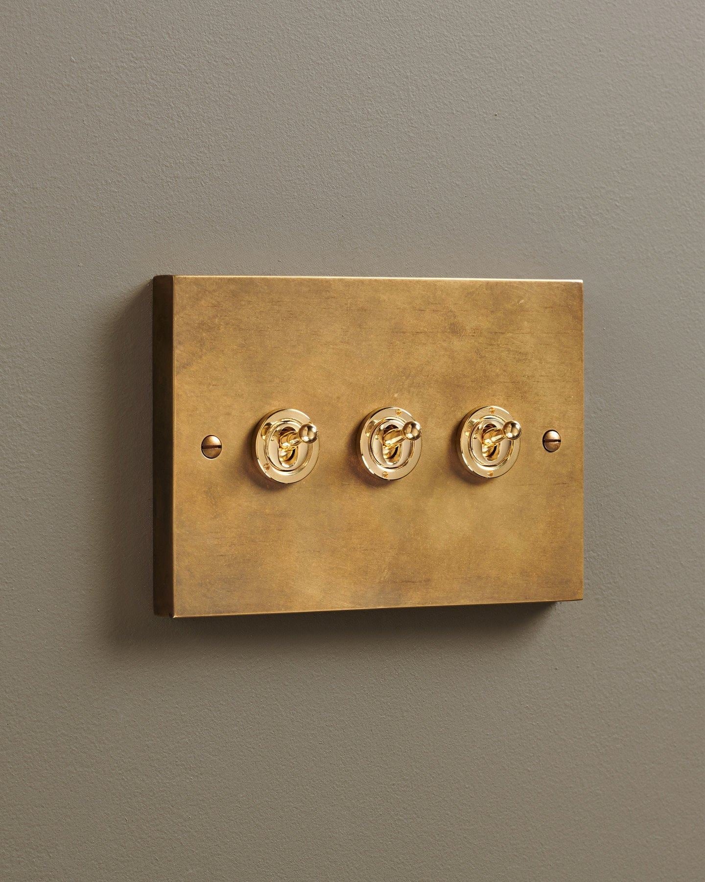 An oblique view of a 3 gang box toggle switch in a warm burnished brass finish.