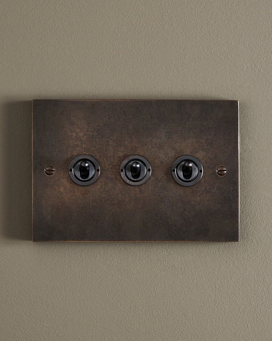 A straight-on view of a 3 gang box toggle switch in a dark oxidised brass finish.