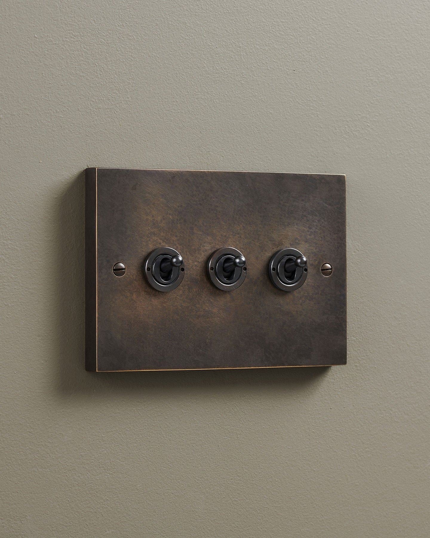 An oblique view of a 3 gang box toggle switch in a dark oxidised brass finish.