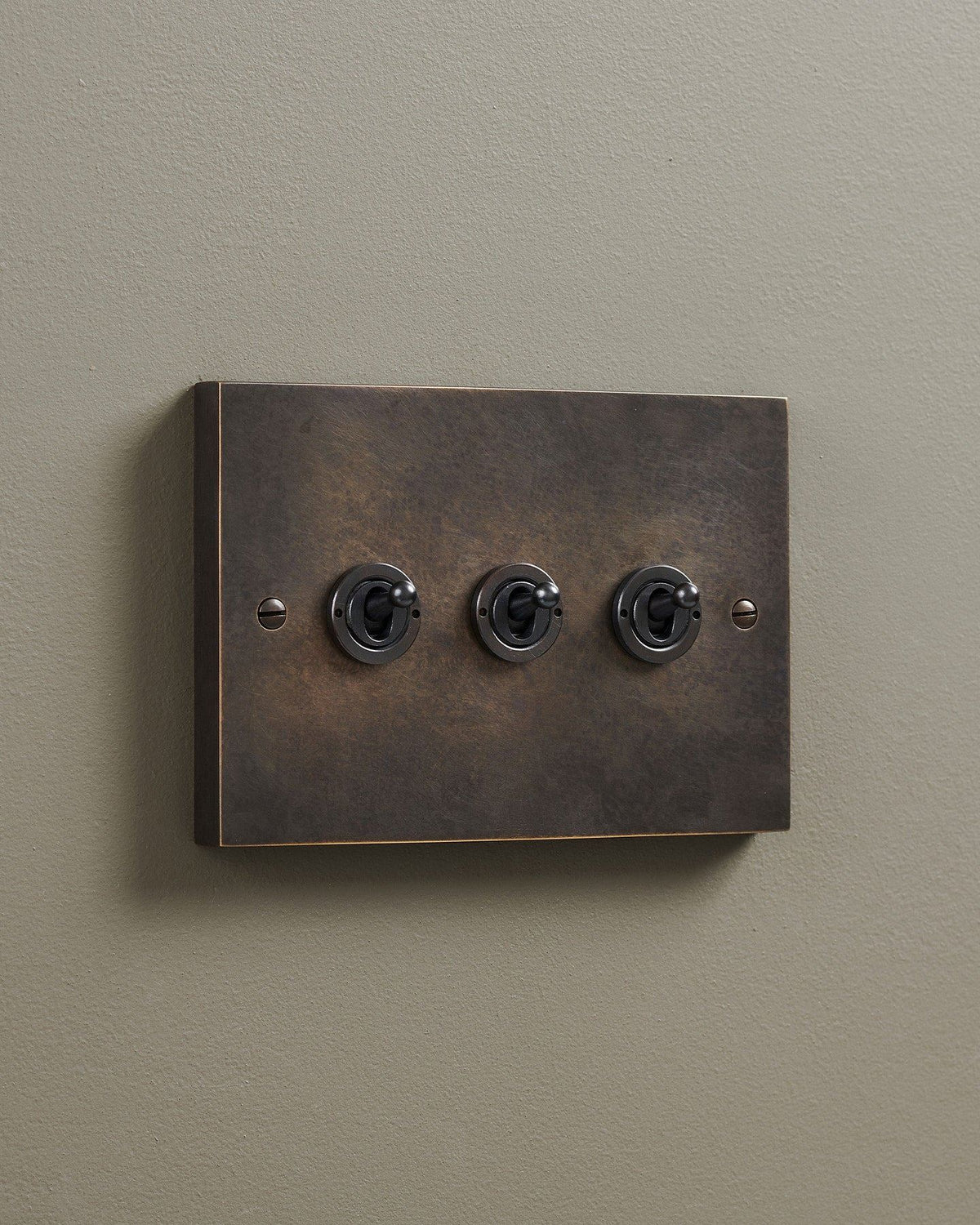 An oblique view of a 3 gang box toggle switch in a dark oxidised brass finish. TEST