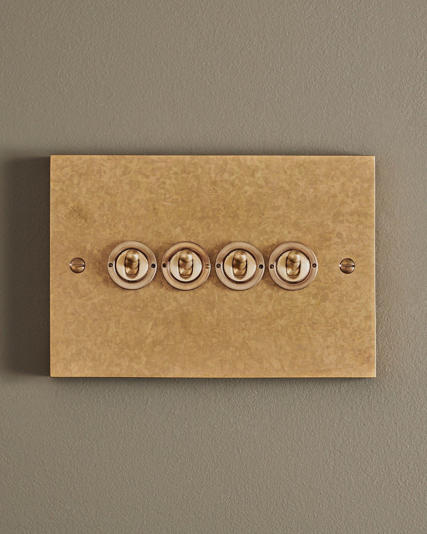A straight-on view of a 4 gang box toggle switch in a mottled aged brass finish.