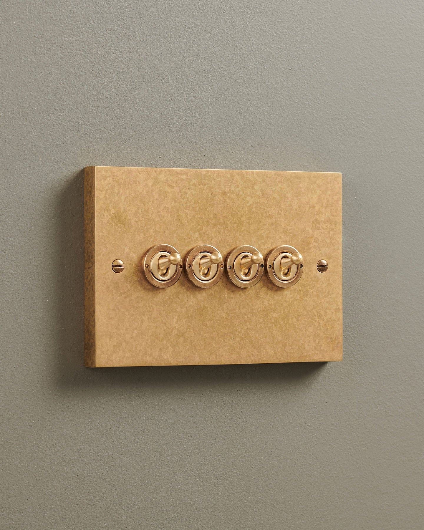 An oblique view of a 4 gang box toggle switch in a mottled aged brass finish.