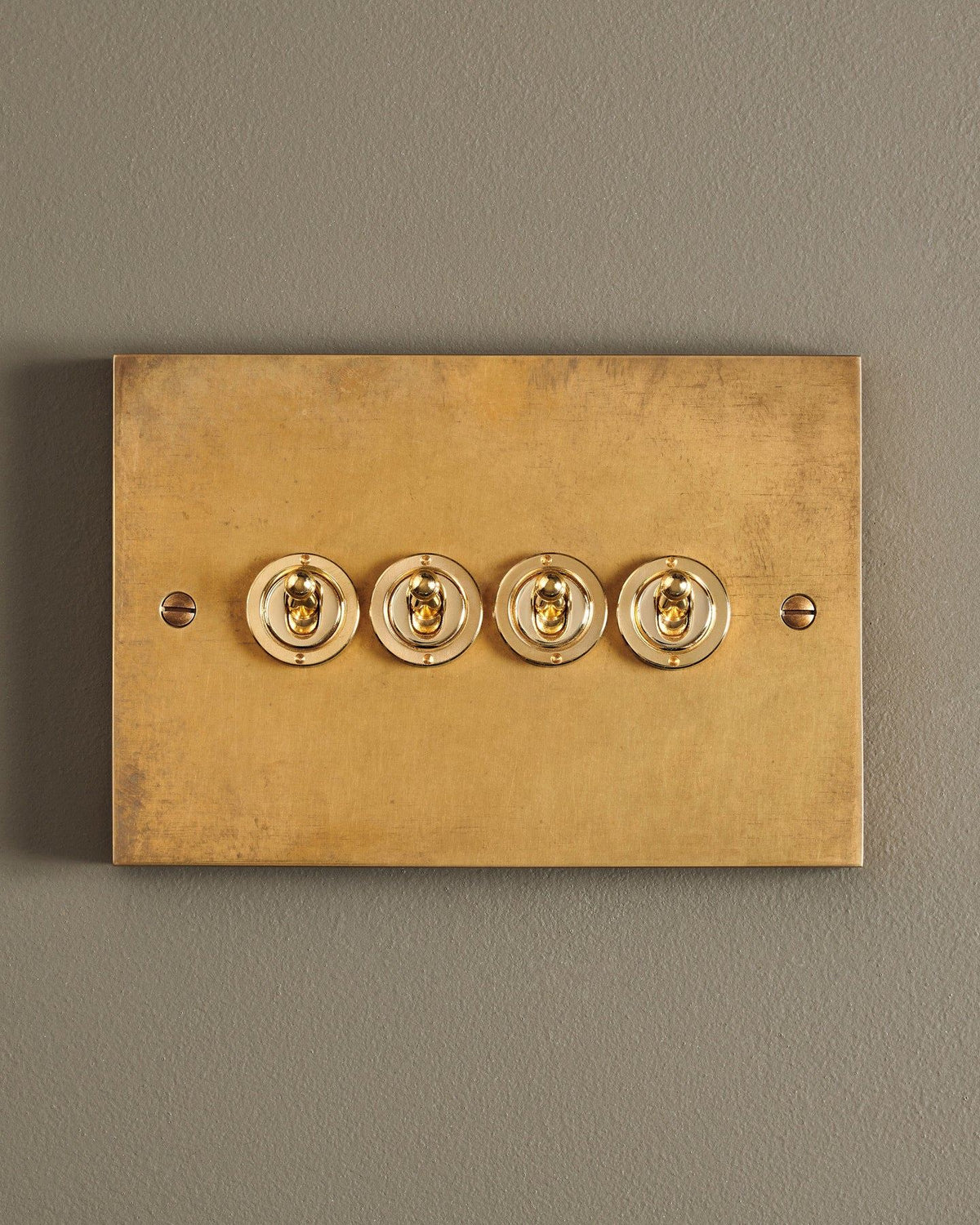 A straight-on view of a 4 gang box toggle switch in a warm burnished brass finish. TEST