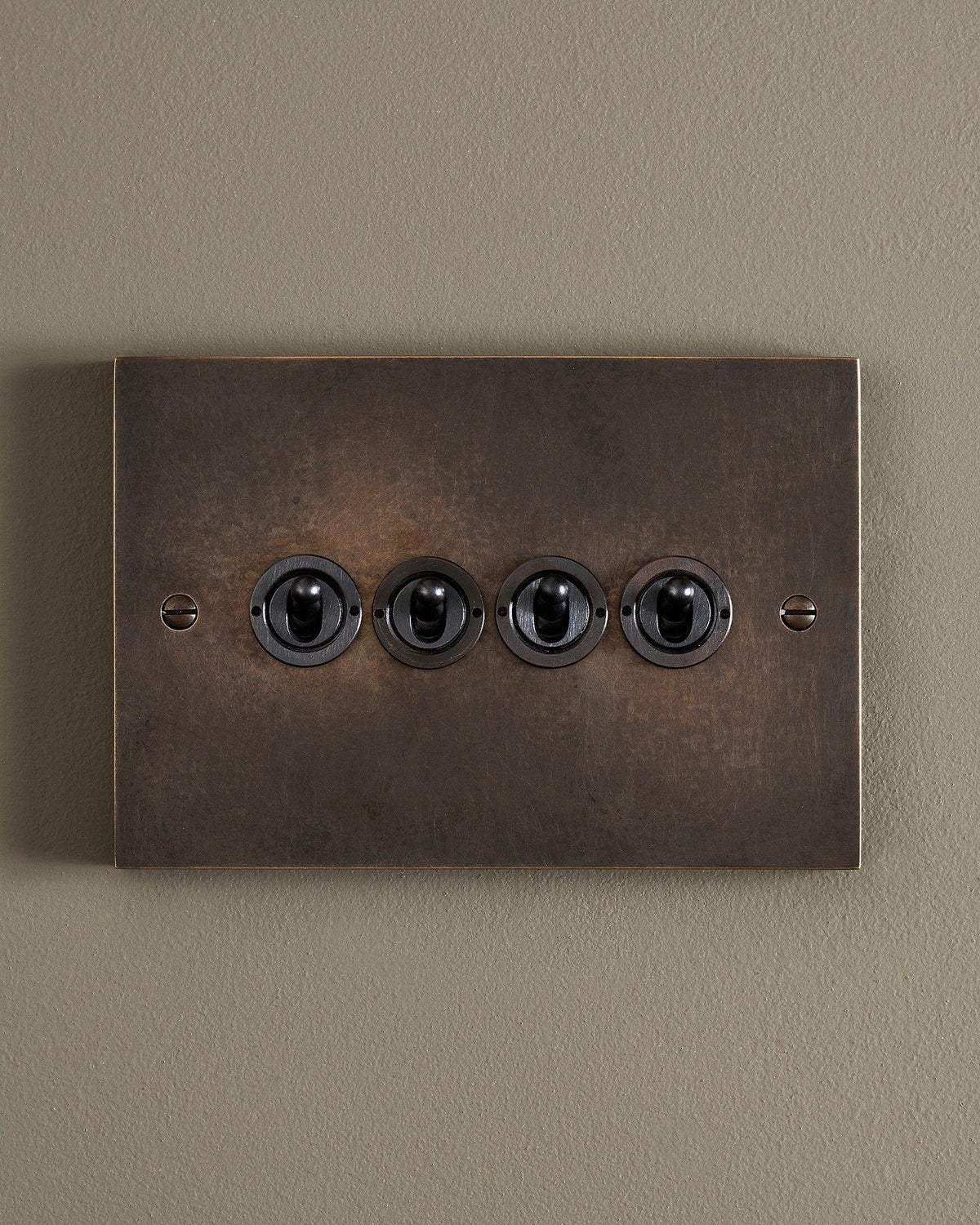 A straight-on view of a 4 gang box toggle switch in a dark oxidised brass finish. TEST