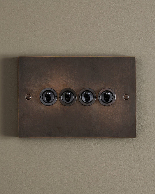 A straight-on view of a 4 gang box toggle switch in a dark oxidised brass finish.