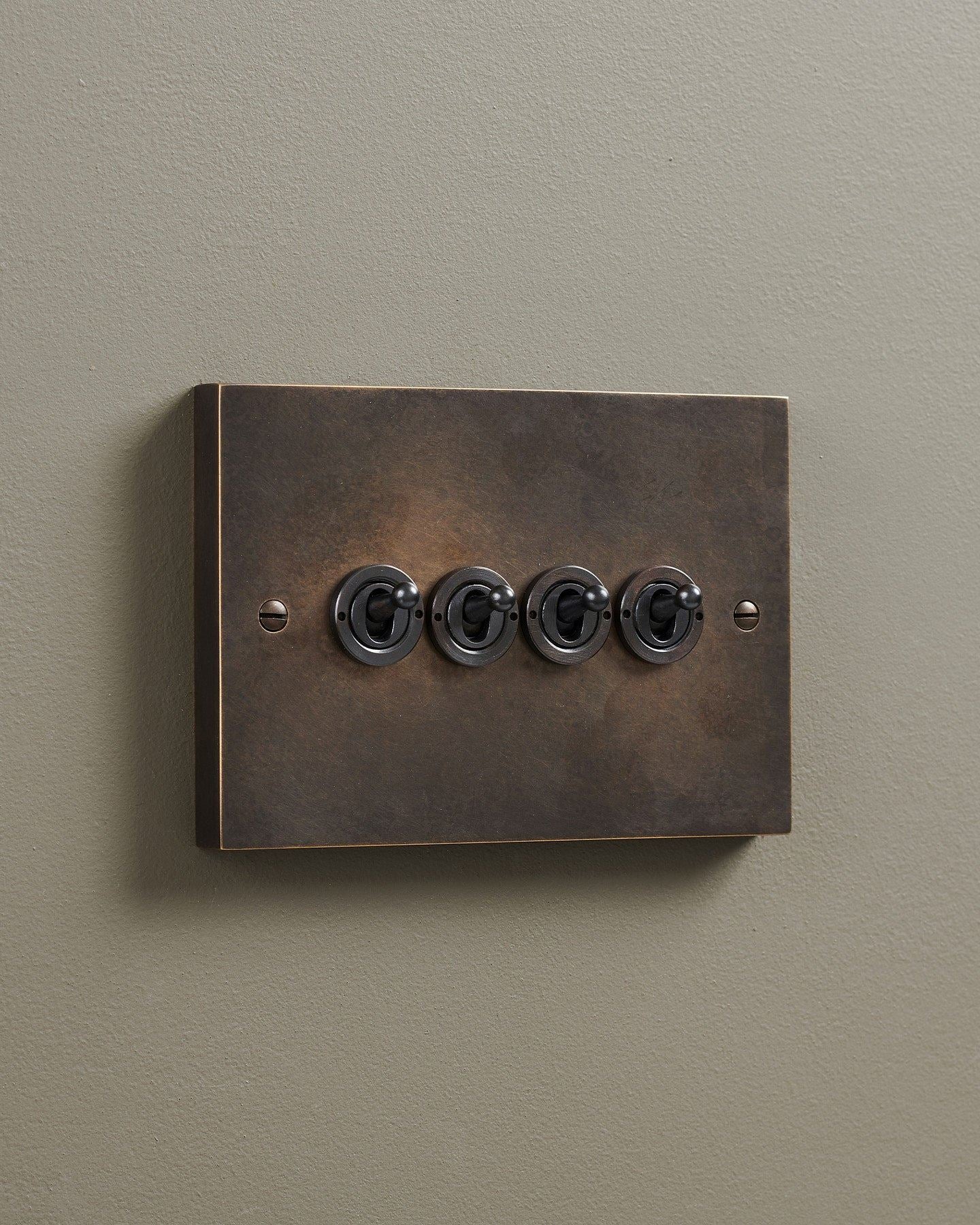 An oblique view of a 4 gang box toggle switch in a dark oxidised brass finish.