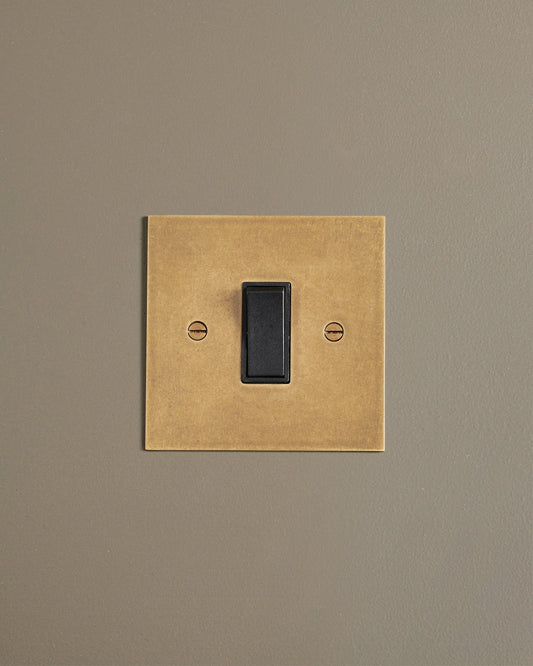 A straight-on view of a classic 20 amp switch in a mottled aged brass finish.