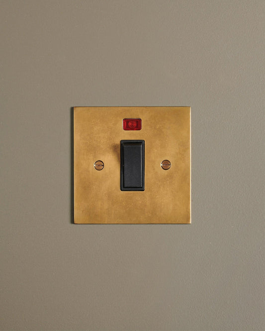 A straight-on view of a classic 32 amp cooker switch in a warm burnished brass finish.