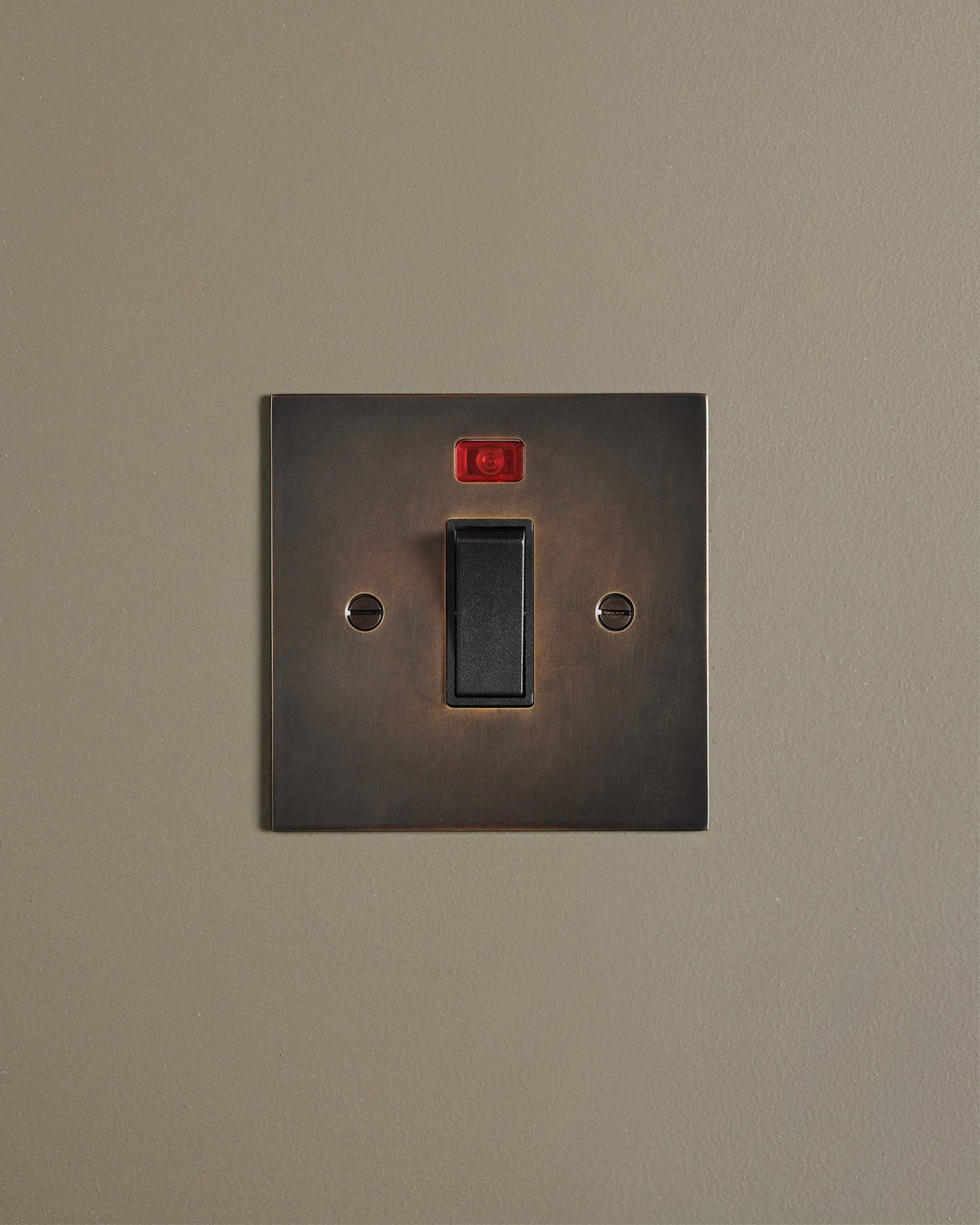 A straight-on view of a classic 32 amp cooker switch in a dark oxidised brass finish. TEST
