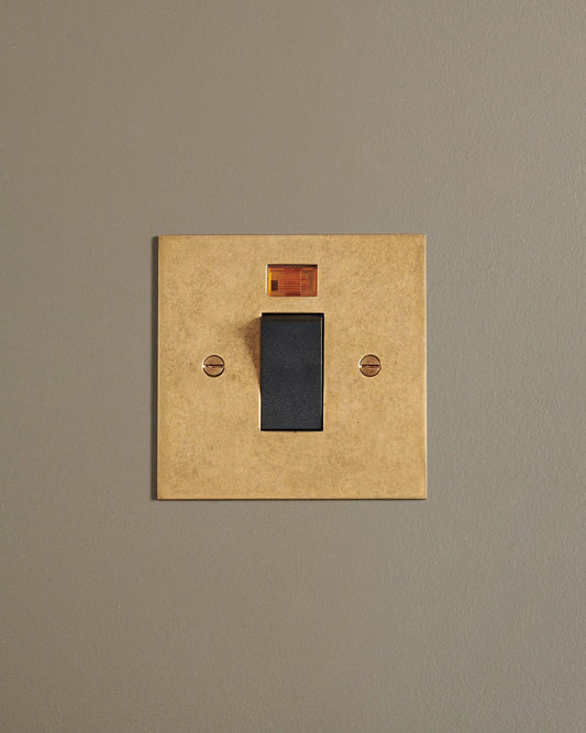 A straight-on view of a classic 45 amp cooker switch in a mottled aged brass finish.