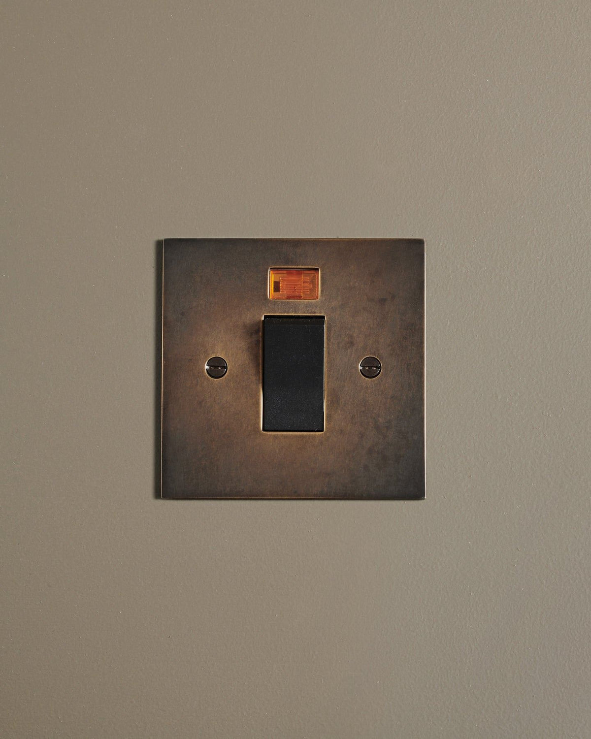 A straight-on view of a classic 45 amp cooker switch in a dark oxidised brass finish. TEST