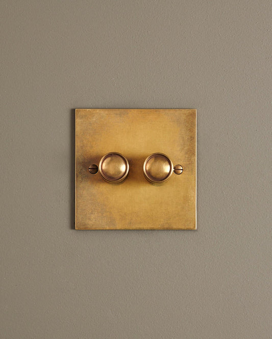 A straight-on view of a 2 gang classic dimmer switch in a warm burnished brass finish.
