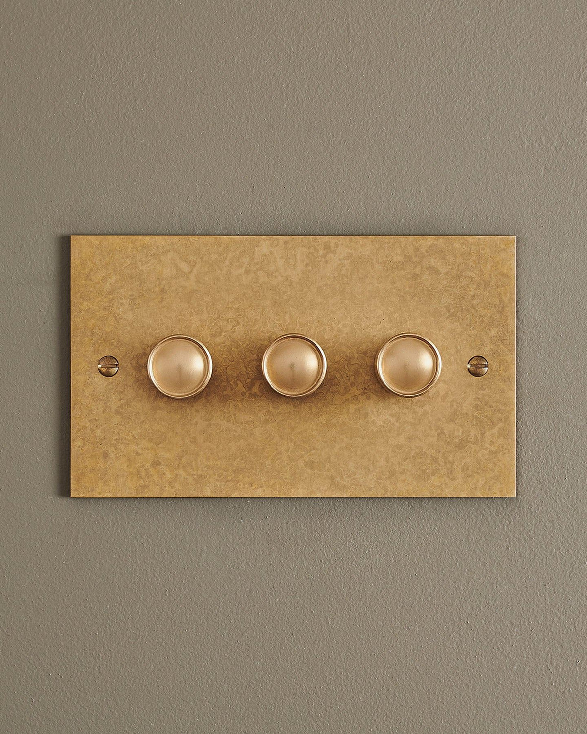 A straight-on view of a 3 gang classic dimmer switch in a mottled aged brass finish. TEST