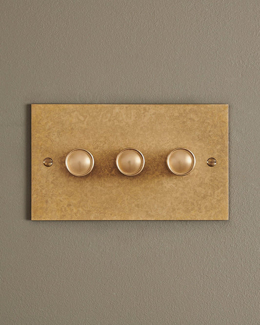 A straight-on view of a 3 gang classic dimmer switch in a mottled aged brass finish.