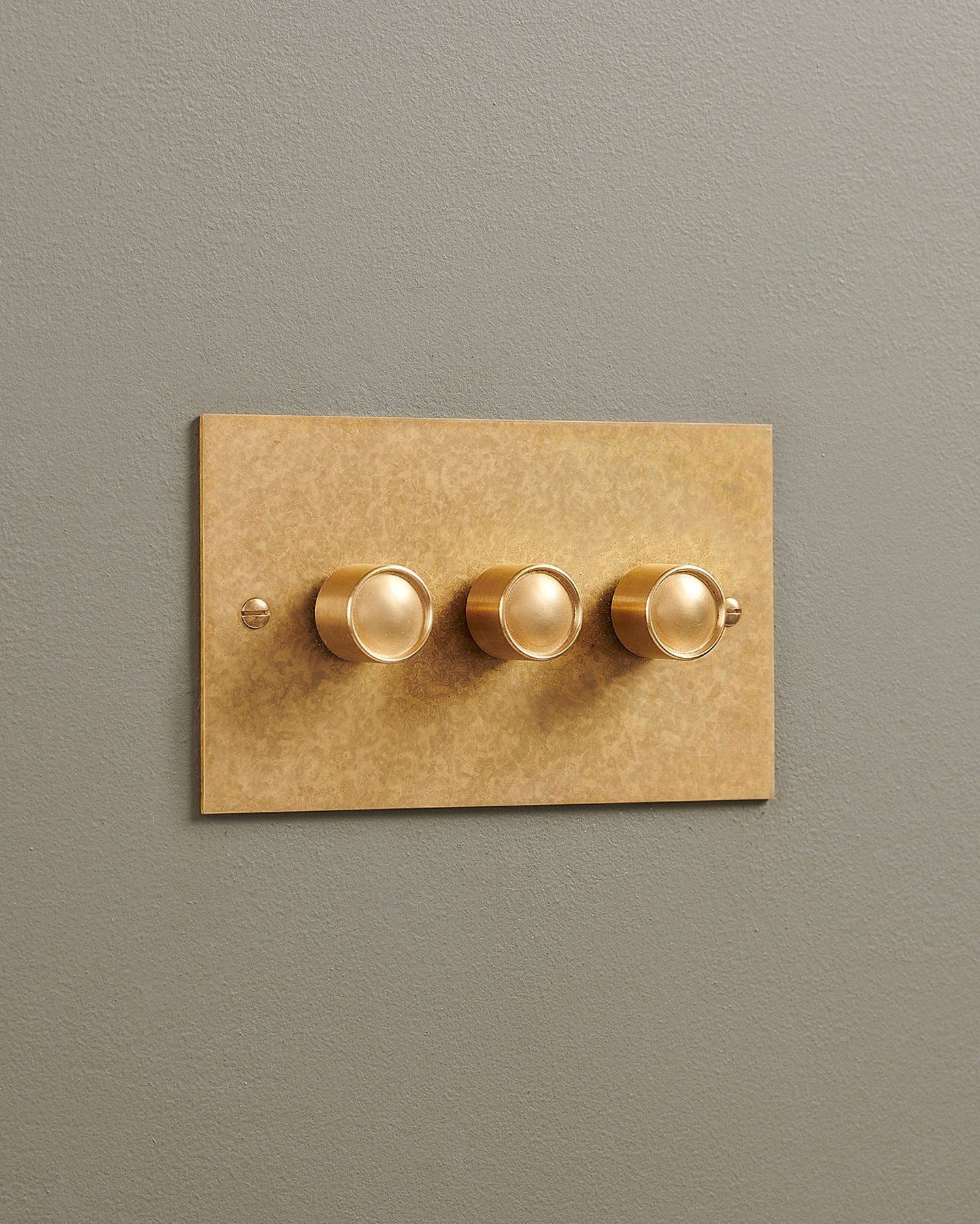 An oblique view of a 3 gang classic dimmer switch in a mottled aged brass finish.