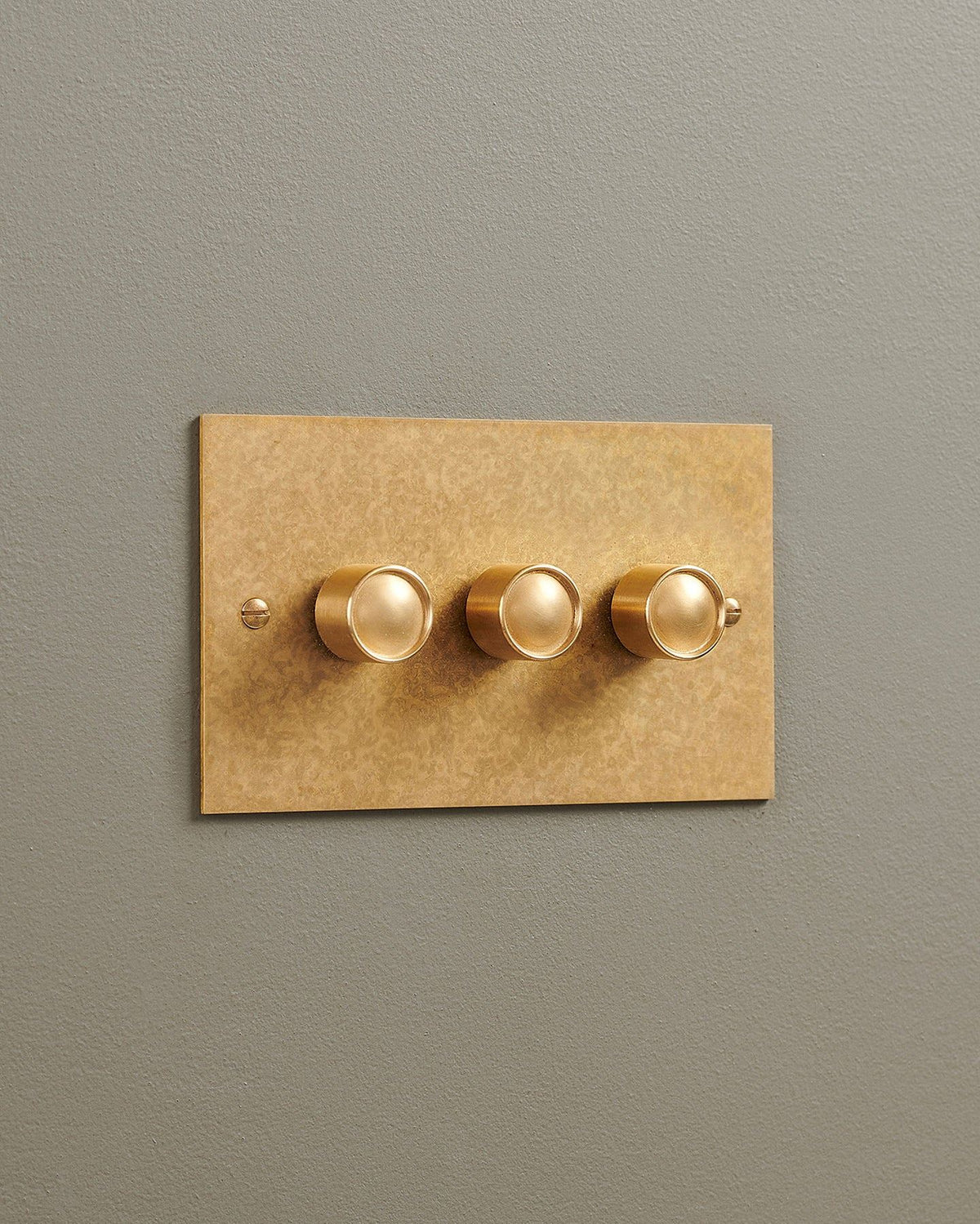 An oblique view of a 3 gang classic dimmer switch in a mottled aged brass finish. TEST
