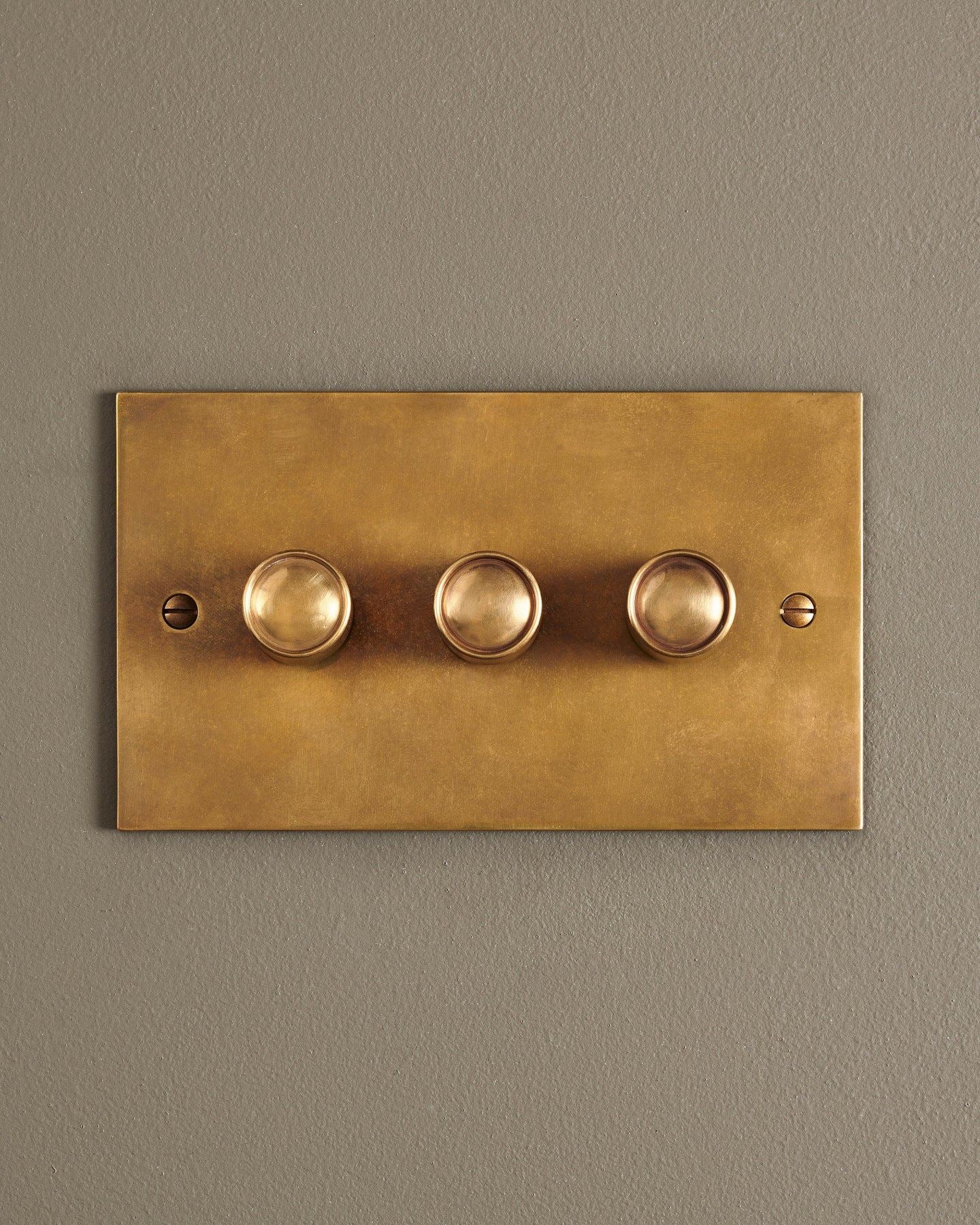 A straight-on view of a 3 gang classic dimmer switch in a warm burnished brass finish.