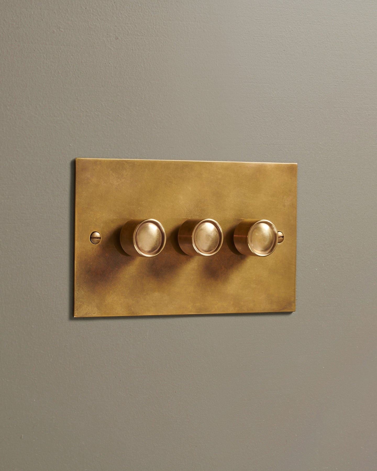 An oblique view of a 3 gang classic dimmer switch in a warm burnished brass finish.