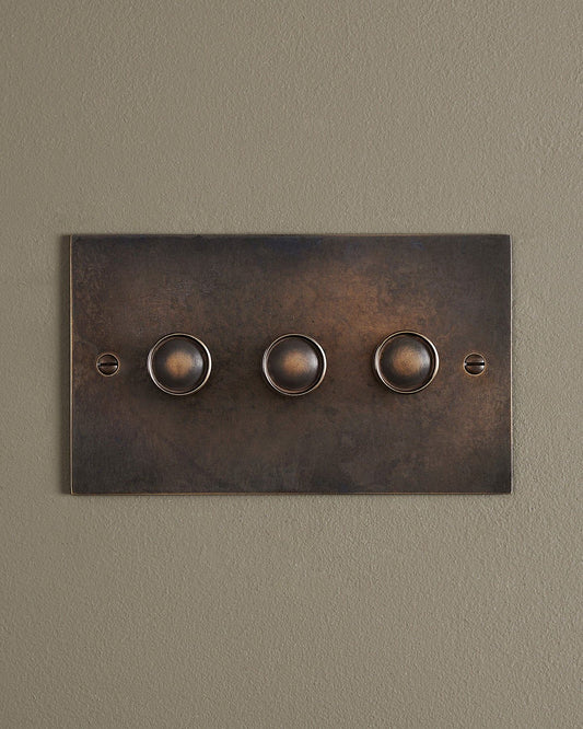 A straight-on view of a 3 gang classic dimmer switch in a dark oxidised brass finish.