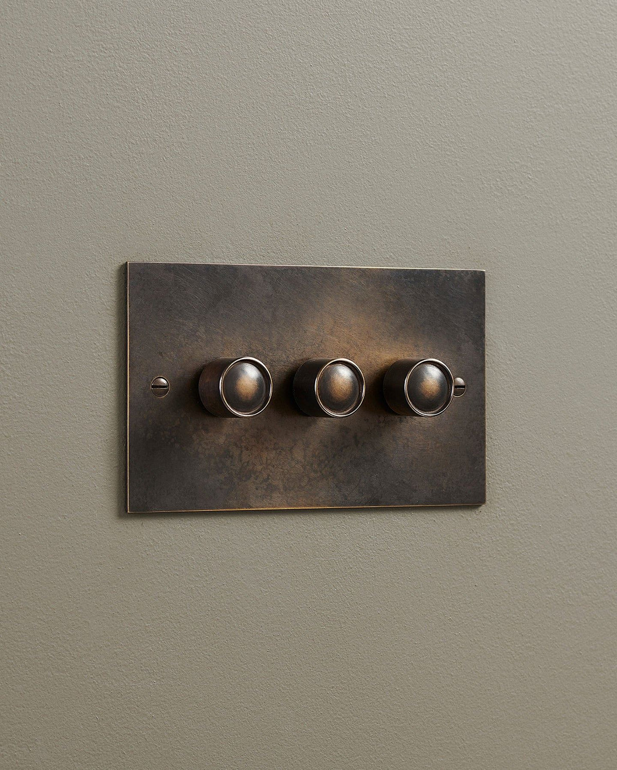 An oblique view of a 3 gang classic dimmer switch in a dark oxidised brass finish. TEST