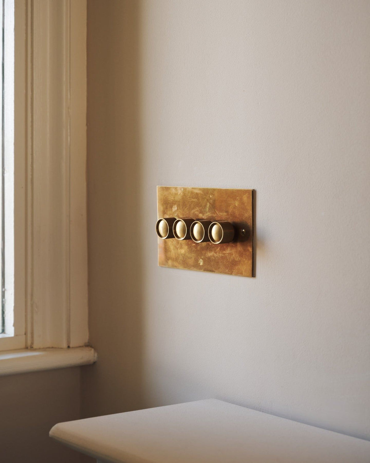 An oblique view of a 4 gang classic dimmer switch in a warm burnished brass finish on soft pink walls with light painted woodwork. | 4 Gang shown TEST