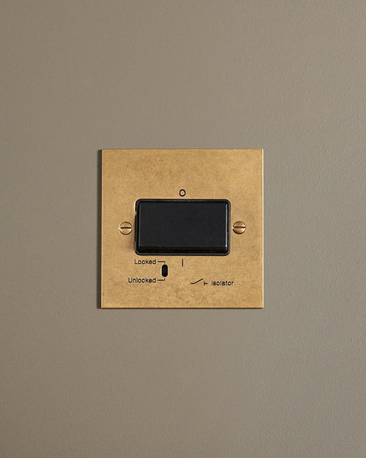 A straight-on view of a classic extractor fan isolator switch a mottled aged brass finish.