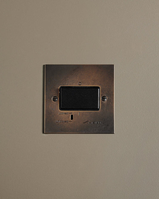 A straight-on view of a classic extractor fan isolator switch a dark oxidised brass finish.