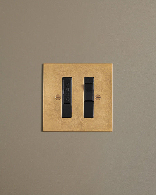 A straight-on view of a classic fused connection switch in a mottled aged brass finish.