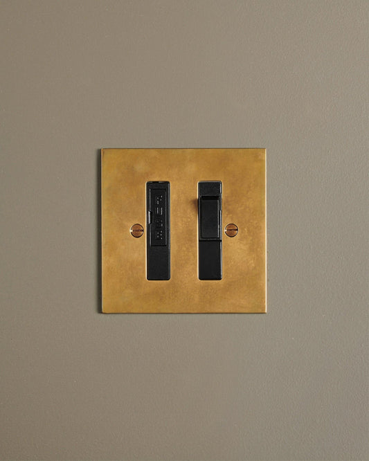 A straight-on view of a classic fused connection switch in a warm burnished brass finish.