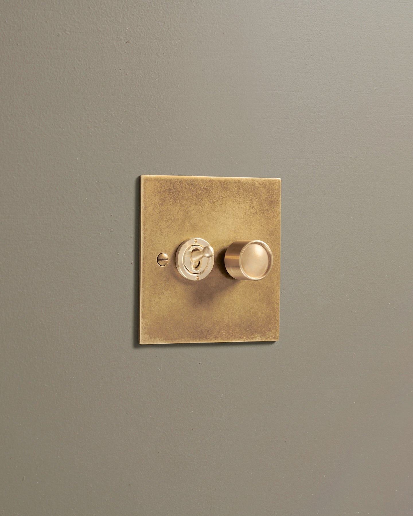 An oblique view of a 2 gang classic toggle and dimmer mixed switch in a mottled aged brass finish.