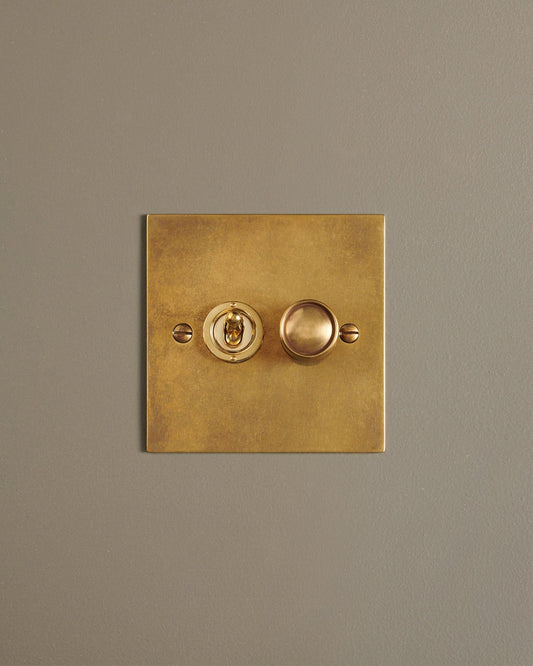 A straight-on view of a 2 gang classic toggle and dimmer mixed switch in a warm burnished brass finish.