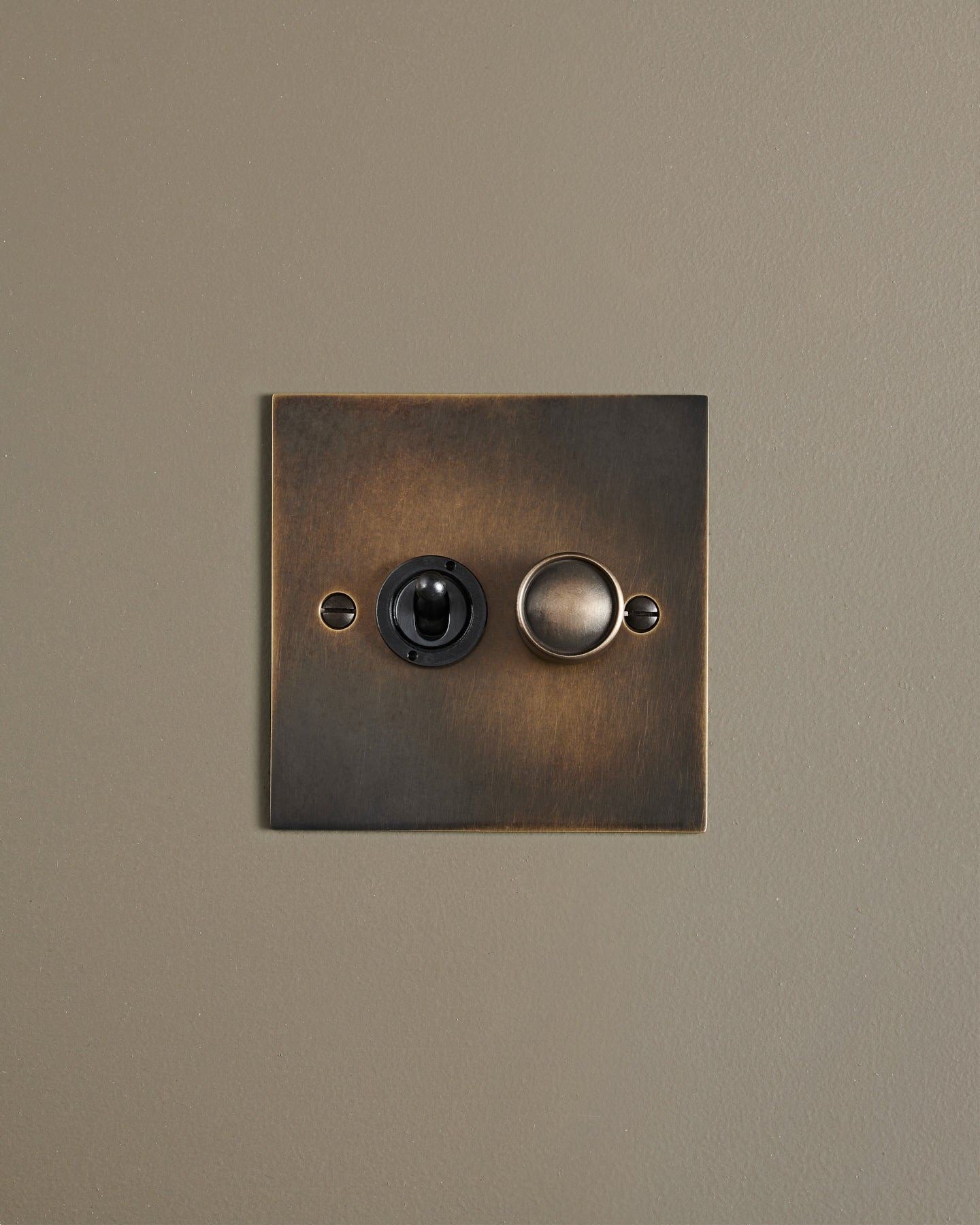 A straight-on view of a 2 gang classic toggle and dimmer mixed switch in a dark oxidised brass finish.