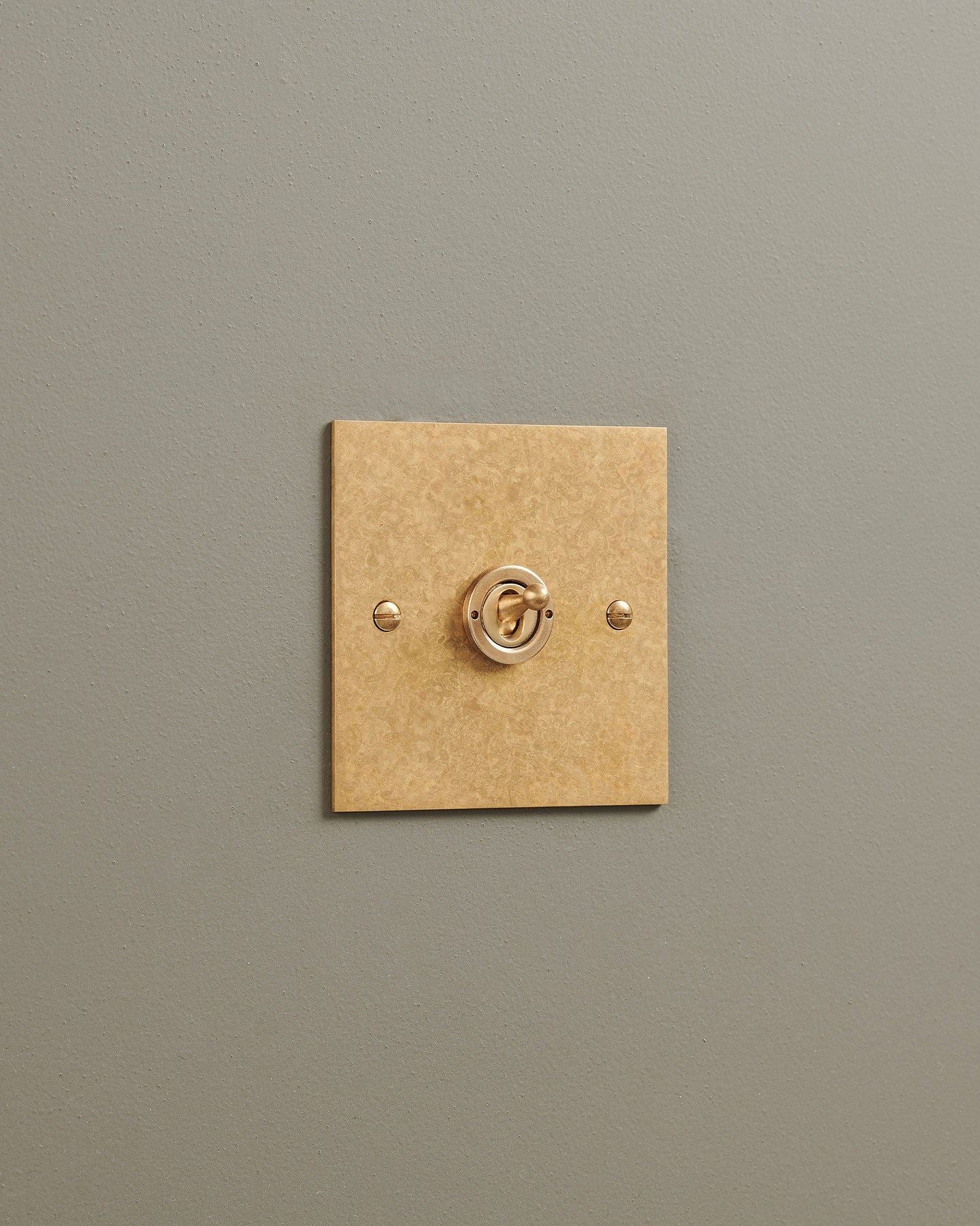An oblique view of a 1 gang classic toggle switch in a mottled aged brass finish.