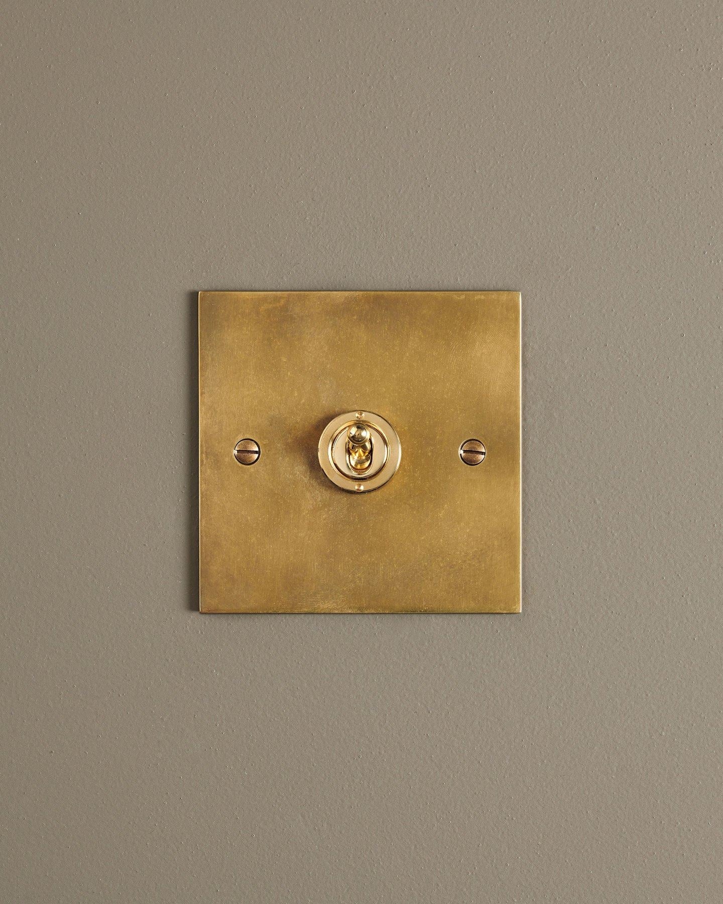 A straight-on view of a 1 gang classic toggle switch in a warm burnished brass finish.