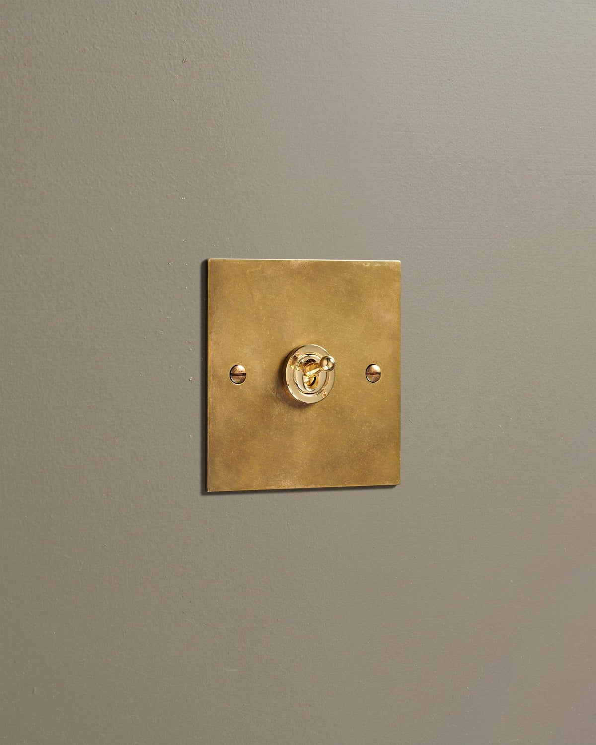 An oblique view of a 1 gang classic toggle switch in a warm burnished brass finish. TEST