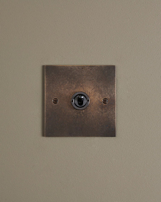 A straight-on view of a 1 gang classic toggle switch in a dark oxidised brass finish.