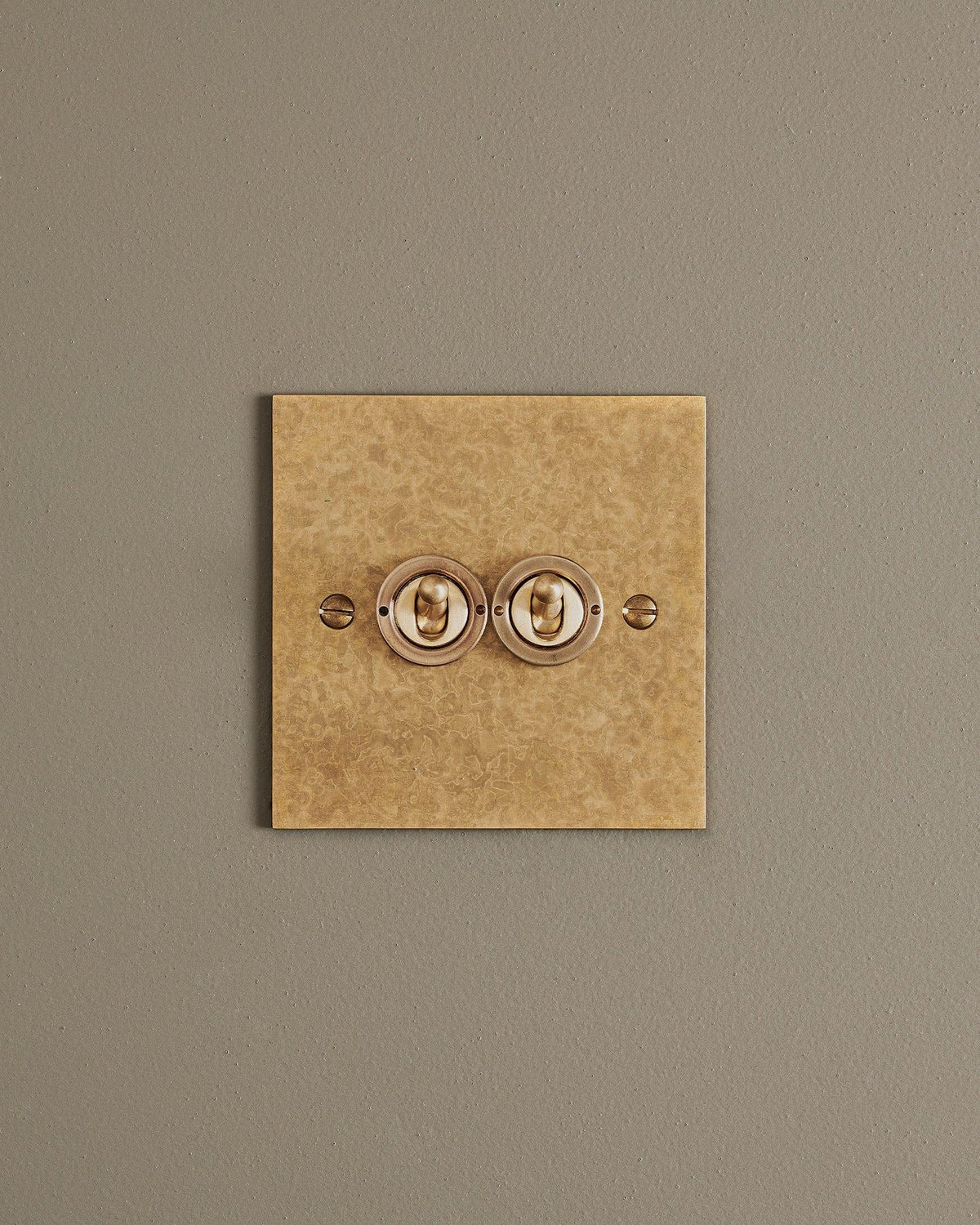 A straight-on view of a 2 gang classic toggle switch in a mottled aged brass finish. TEST