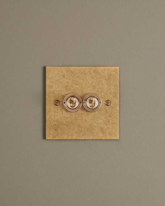 A straight-on view of a 2 gang classic toggle switch in a mottled aged brass finish.