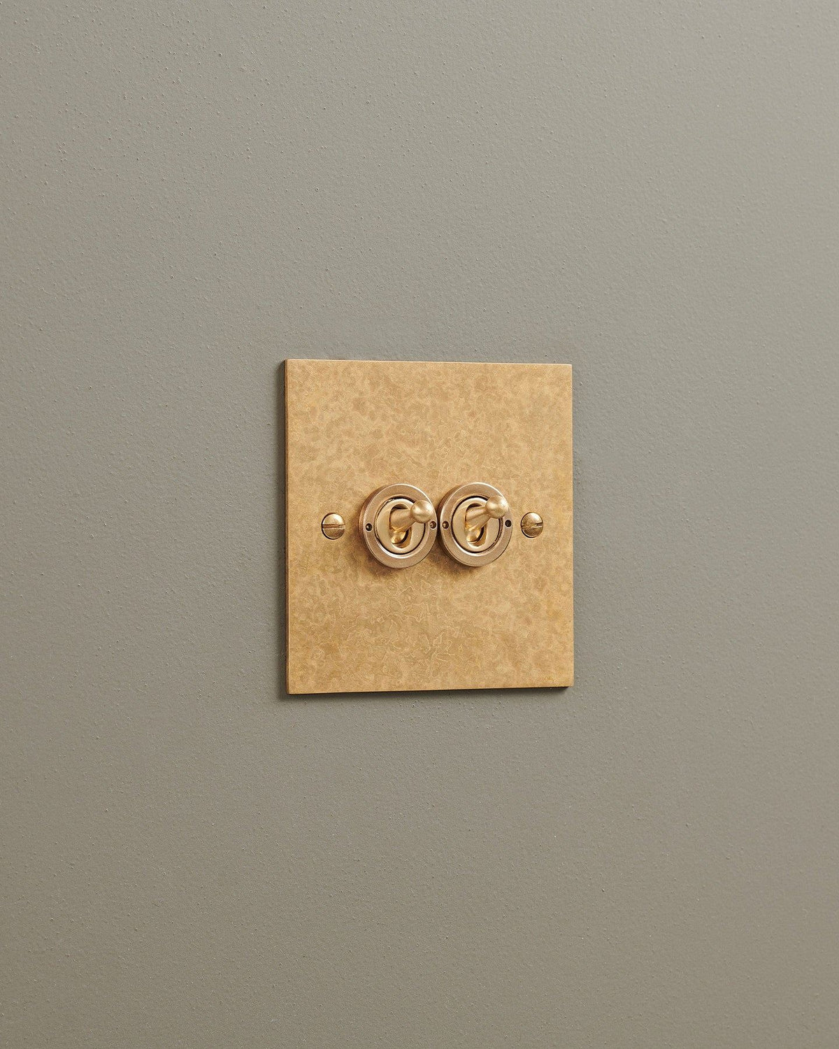 An oblique view of a 2 gang classic toggle switch in a mottled aged brass finish. TEST