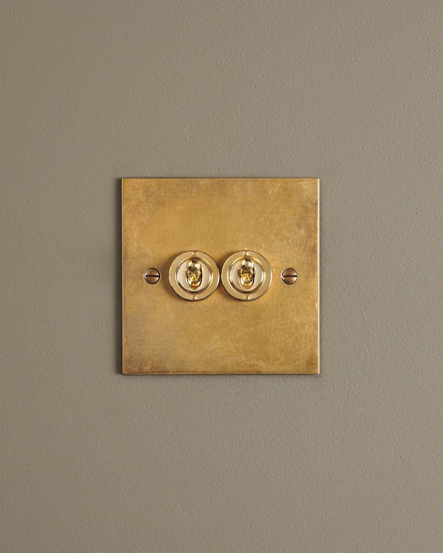 A straight-on view of a 2 gang classic toggle switch in a warm burnished brass finish.