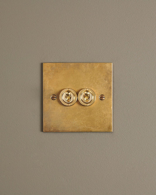 A straight-on view of a 2 gang classic toggle switch in a warm burnished brass finish.