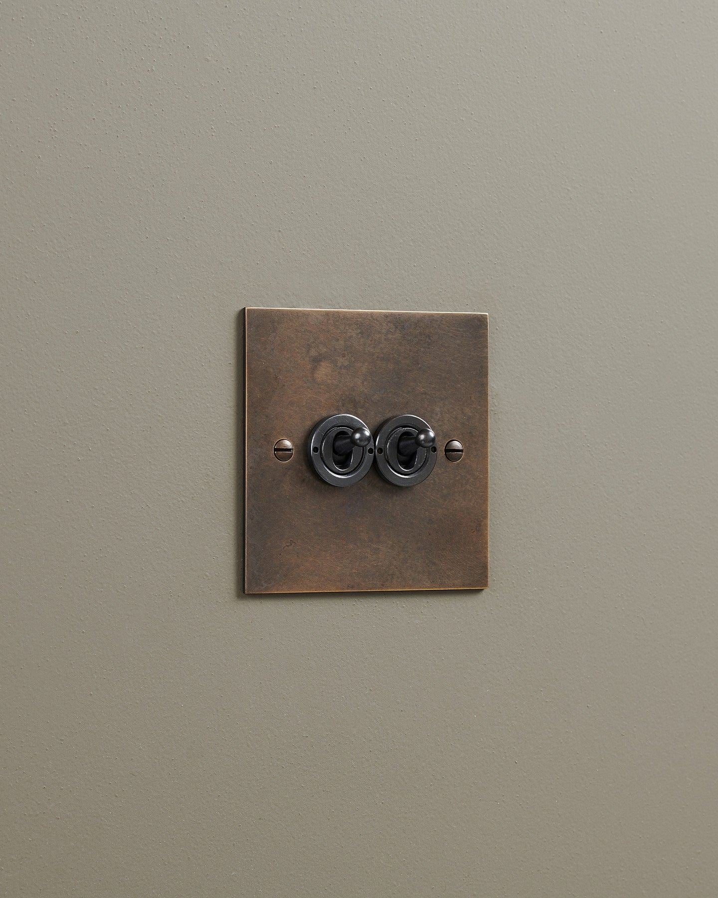An oblique view of a 2 gang classic toggle switch in a dark oxidised brass finish.