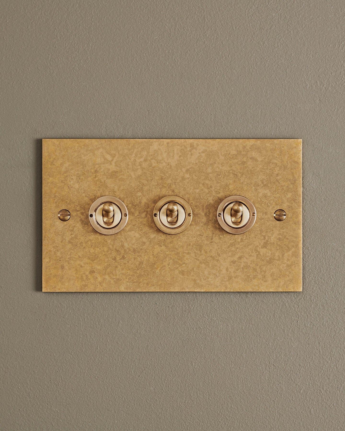 A straight-on view of a 3 gang classic toggle switch in a mottled aged brass finish.
