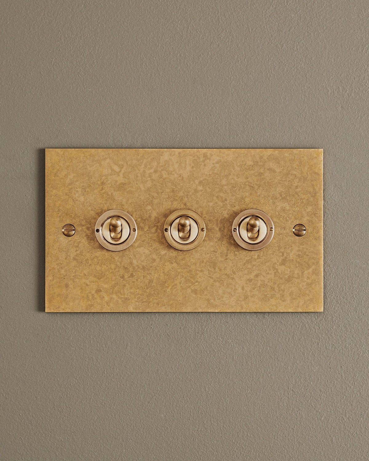 A straight-on view of a 3 gang classic toggle switch in a mottled aged brass finish. TEST