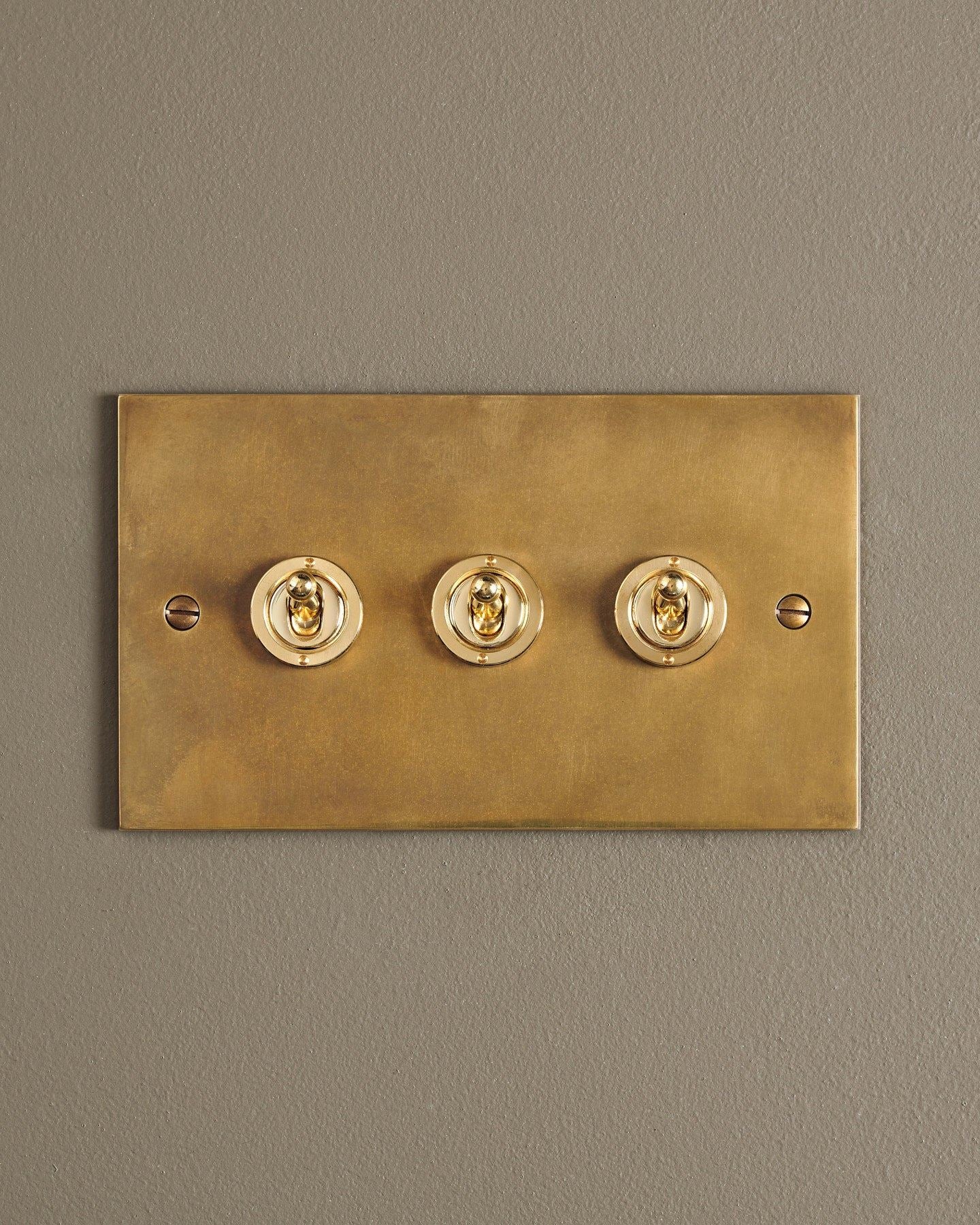 A straight-on view of a 3 gang classic toggle switch in a warm burnished brass finish.