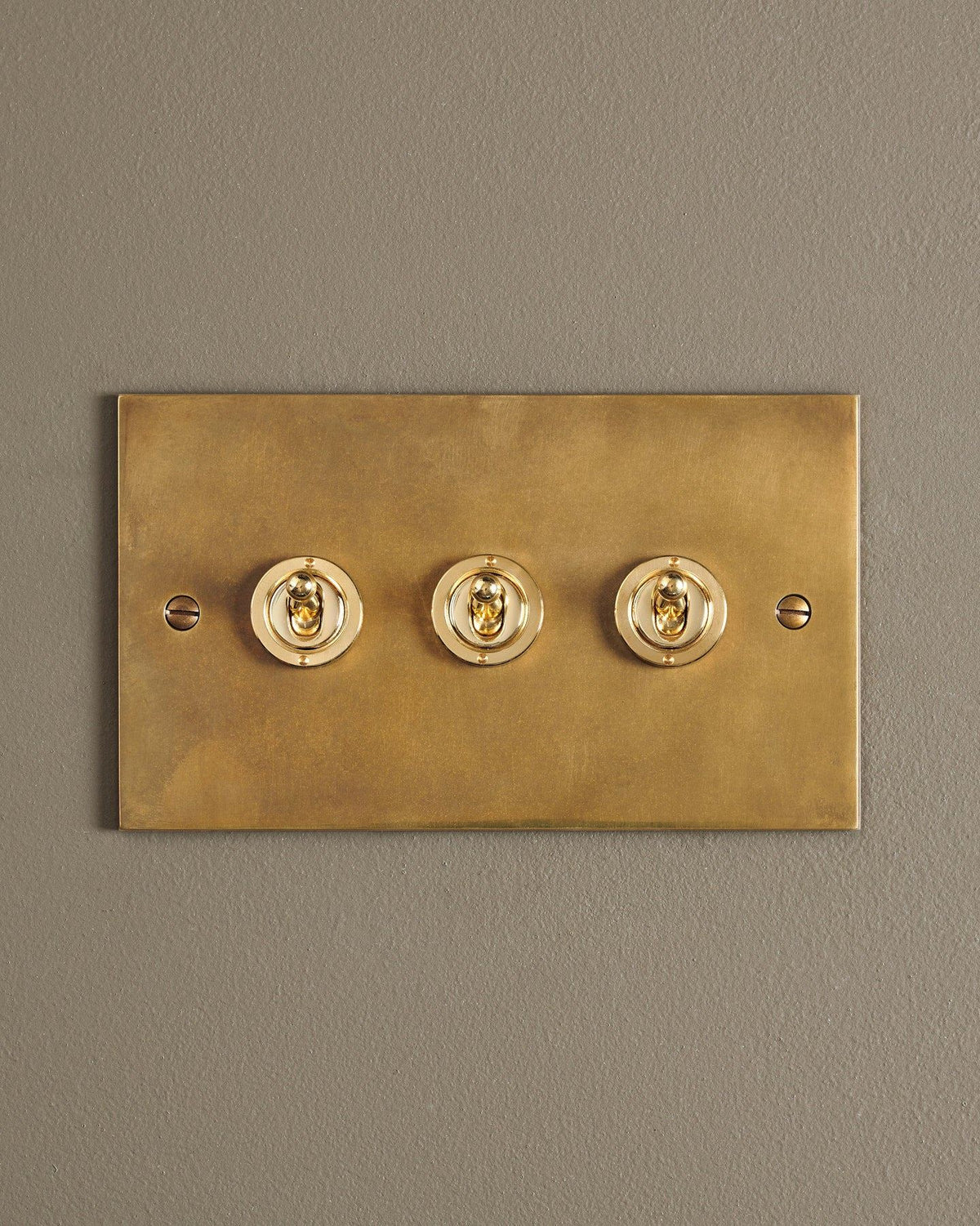 A straight-on view of a 3 gang classic toggle switch in a warm burnished brass finish. TEST
