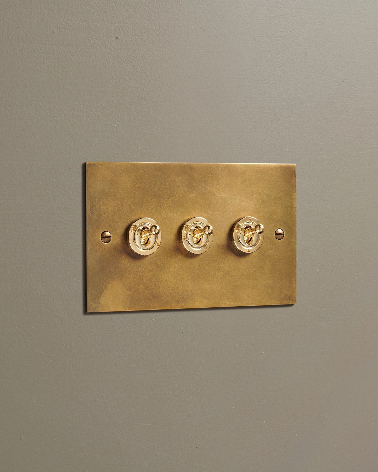An oblique view of a 3 gang classic toggle switch in a warm burnished brass finish.