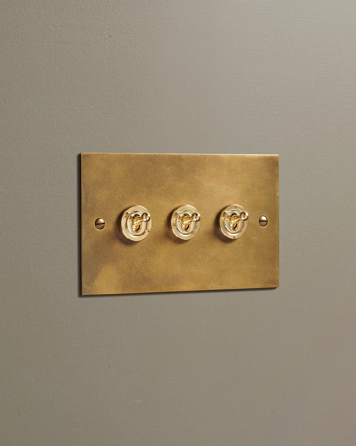 An oblique view of a 3 gang classic toggle switch in a warm burnished brass finish. TEST