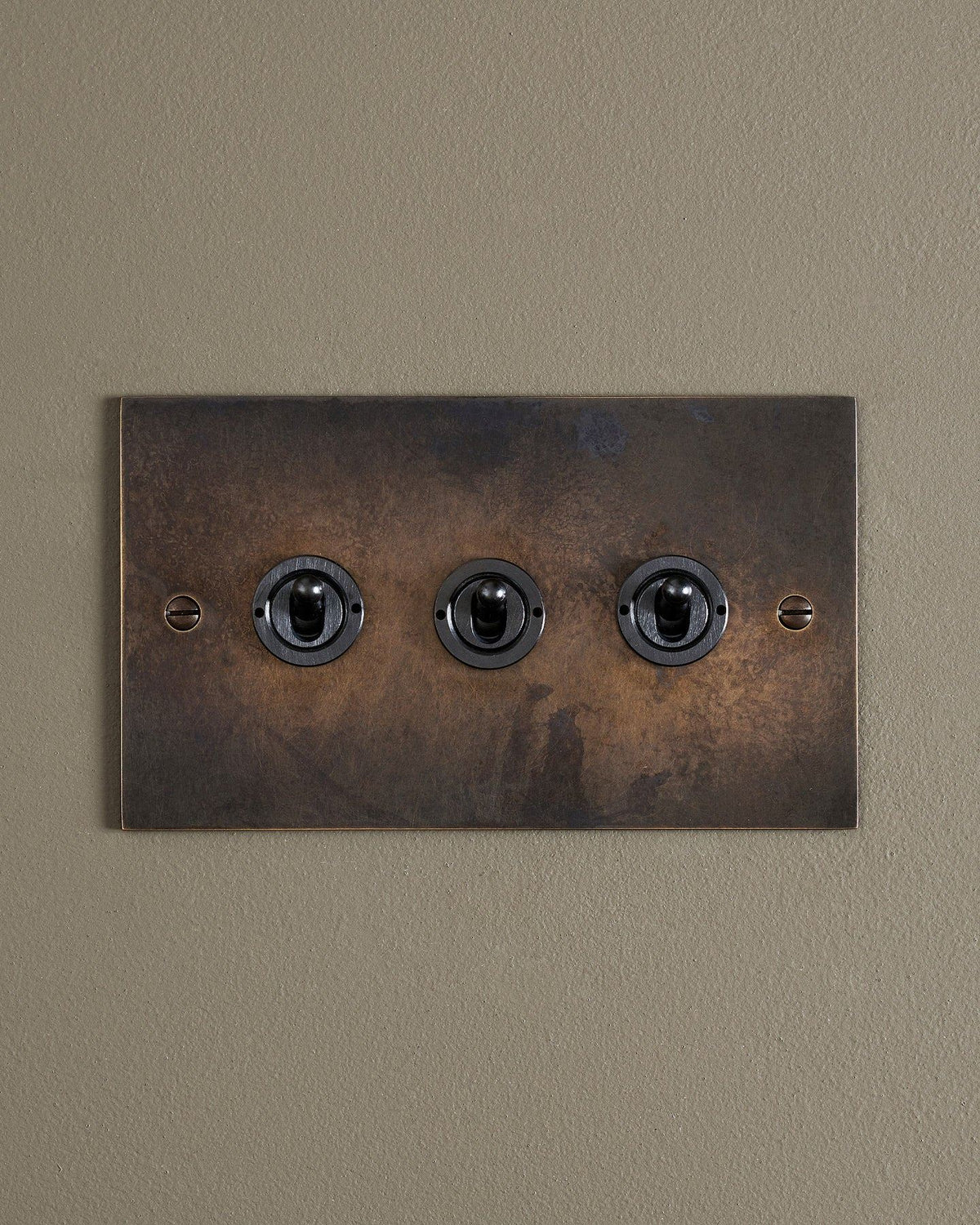 A straight-on view of a 3 gang classic toggle switch in a dark oxidised brass finish. TEST