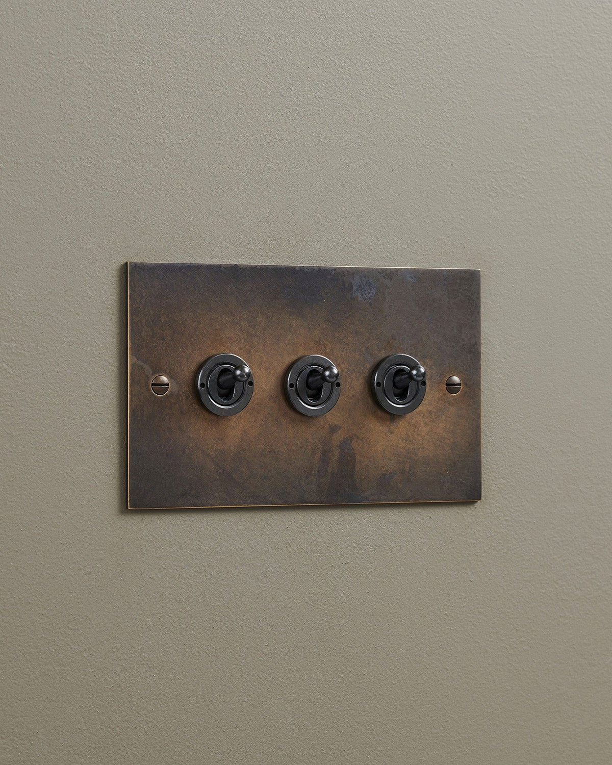 An oblique view of a 3 gang classic toggle switch in a dark oxidised brass finish. TEST